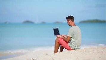 jeune homme avec ordinateur portable sur la plage tropicale des Caraïbes