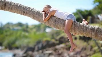 Little girl at tropical beach sitting on palm tree during summer vacation