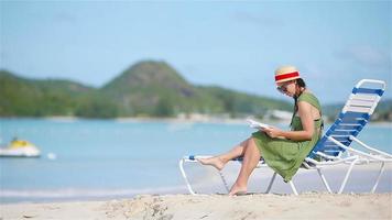 Young woman reading book on sunbeds during tropical white beach