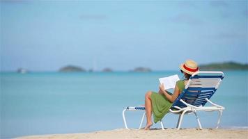 jonge vrouw leesboek op ligbedden tijdens tropisch wit strand