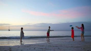 glückliche familie, die bei sonnenuntergang mit fliegender scheibe am strand spielt video