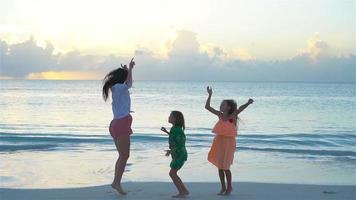 kleine schattige meisjes en jonge moeder op tropisch strand in warme avond dansen en plezier maken. familie bij zonsondergang