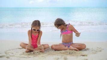 Adorable little girls playing with sand on the beach. Kids sitting in shallow water and making a sandcastle video