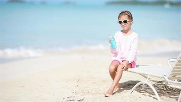 klein schattig meisje met fles zonnebrandcrème zittend op tropisch strand video