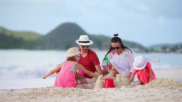 los padres con niños juegan a hacer castillos de arena en la playa blanca tropical