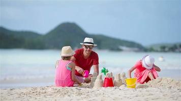 Familie macht Sandburg am tropischen weißen Strand. Vater und zwei Mädchen spielen mit Sand am tropischen Strand
