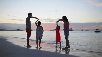 los padres y dos niños se divierten mucho en la playa al atardecer. familia de cuatro enamorados, felices y hermosos. video