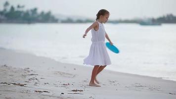niña jugando con disco volador en la playa al atardecer