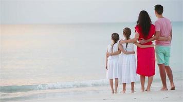 felice bella famiglia sulla spiaggia. vista posteriore di genitori e bambini al tramonto video