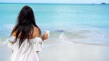 mujer joven con café caliente disfrutando de vistas a la playa. hermosa chica en video en cámara lenta