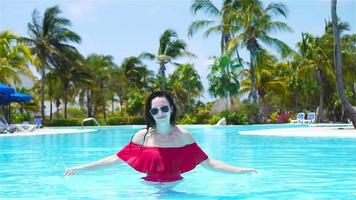 vacker ung kvinna avkopplande i poolen. glad tjej i utomhuspool på lyxhotell video