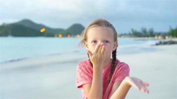 schattig klein meisje op het strand met veel plezier bij zonsondergang. gelukkig kind camera kijken en kussen achtergrond mooie lucht en zee. slow motion video