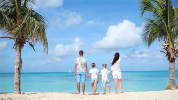 vue arrière d'une famille de quatre personnes en blanc sur la plage en vacances dans les Caraïbes. les parents de deux enfants profitent de leurs vacances dans les Caraïbes sur l'île d'antigua