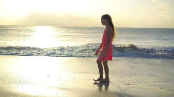 sihouette van een klein meisje dat bij zonsondergang op het strand loopt. video