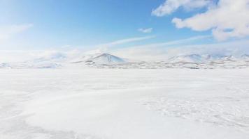 Vergrößern Sie die aufsteigende Ansicht der eisigen Seeoberflächenstruktur mit Berghintergrund. Winterwunderland-Naturbanner video