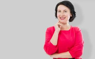 Smiling Middle age woman in red dress and crossed arms isolated on gray background. Make up and beauty concept. Copy space photo