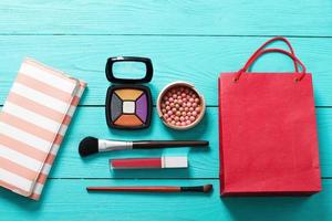 maquillaje cosmético y accesorios con bolsa roja sobre fondo de madera azul. vista superior y maqueta. foto