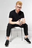 Young man on a chair, Portrait of handsome young man sitting on a chair, Proud and satisfied young man sitting on chair and looking at camera isolated, Casual young man in glasses photo