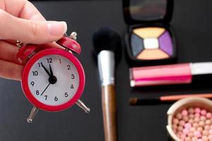 Concept cropped image with cosmetic and make up products. Quick make-up. Red retro clock. Selective focus photo