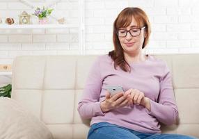 mujer de mediana edad usando un teléfono inteligente en el fondo de casa. copia espacio y maqueta. compras en línea, tecnología de Internet en el teléfono celular. foto