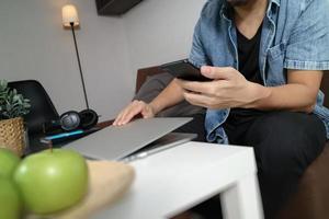 Mano de diseñador usando computadora portátil y compras en línea de pagos móviles, omnicanal, sentado en un sofá en la sala de estar, manzanas verdes en una bandeja de madera foto