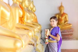 atractiva mujer tailandesa con un antiguo vestido tailandés sostiene una guirnalda de flores frescas que rinden homenaje a buda para pedir un deseo en el festival tradicional de songkran en tailandia foto