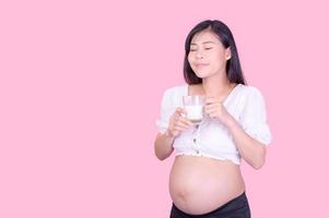 A beautiful pregnant woman standing and drinking fresh milk for good health for her future baby photo
