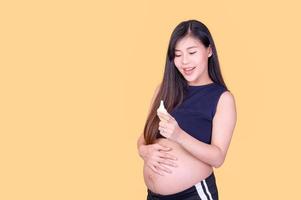 A beautiful pregnant Asian woman touches her belly and uses an ear thermometer to measure the fever photo