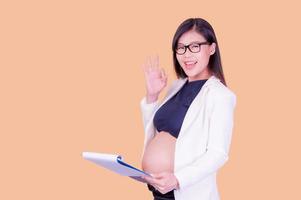 A beautiful pregnant Asian woman holding a paper binder, relaxing and enjoying her work photo