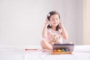 una linda chica asiática está felizmente usando una tableta para escuchar música y aprender en el dormitorio foto