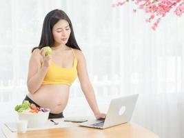 una mujer embarazada en una habitación japonesa busca en Internet información sobre frutas y verduras para comer para la salud foto