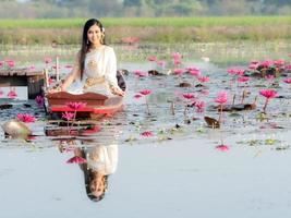 An elegant Thai woman wearing traditional Thai clothes adorned with gold ornaments, sitting on a wooden boat floating in a lotus field photo