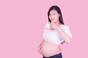 A beautiful pregnant woman standing and drinking fresh milk for good health for her future baby photo