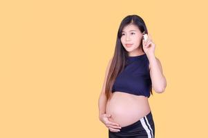 A beautiful pregnant Asian woman touches her belly and uses an ear thermometer to measure the fever photo