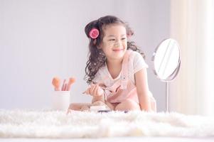 una linda niña asiática está felizmente aplicando pinceles de maquillaje con polvo en su dormitorio