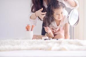 A cute Asian girl has fun applying makeup powder in her bedroom while the beautician does her hair photo