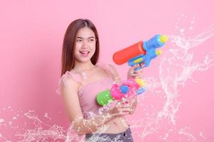 una hermosa mujer asiática muestra un gesto mientras sostiene una pistola de agua de plástico durante el festival songkran foto