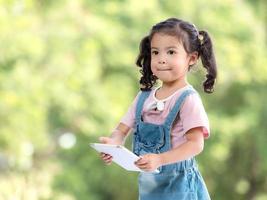 A cute Asian girl is using a tablet for fun playing games and learning outside of school in the park photo