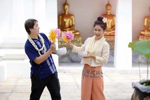 Young Thai men and women in traditional Thai dress hold flowers splashing water for fun at the Songkran water festival photo