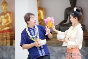 jóvenes tailandeses, hombres y mujeres vestidos con ropa tradicional tailandesa, sostienen flores salpicando agua para divertirse en el festival del agua de songkran foto