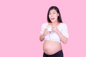 una hermosa mujer embarazada de pie y bebiendo leche fresca para la buena salud de su futuro bebé foto