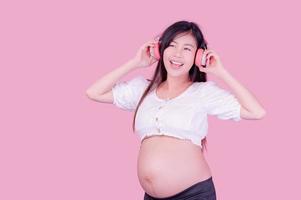 Asian beautiful pregnant woman stands relaxed and enjoys listening to music on headphones connected to the internet photo