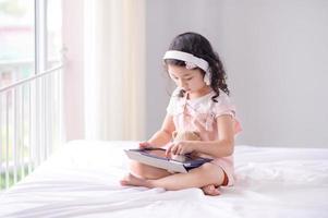 una linda chica asiática está usando una tableta para divertirse jugando y aprendiendo en la habitación