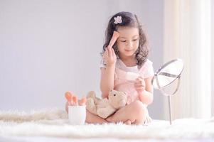 una linda niña asiática está felizmente aplicando pinceles de maquillaje con polvo en su dormitorio