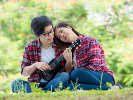 Asian female couples LGBT sitting and playing ukulele in the garden and embrace each other in love and happiness