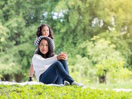 niña asiática sentada con su madre en la alfombra, relajándose y aprendiendo fuera de la escuela para disfrutar en el parque natural