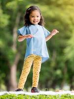 niña asiática parada en la alfombra, jugando y aprendiendo fuera de la escuela para disfrutar en el parque natural foto