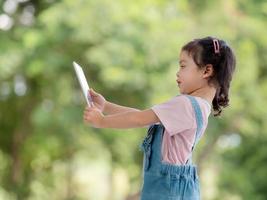 una linda chica asiática está usando una tableta para divertirse jugando y aprendiendo fuera de la escuela en el parque foto