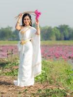 una elegante mujer tailandesa con ropa tradicional tailandesa que lleva flores de loto recolectadas en un campo de loto foto