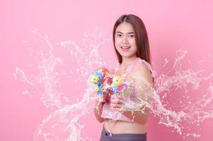 A beautiful Asian woman shows a gesture while holding a plastic water gun during the Songkran festival photo